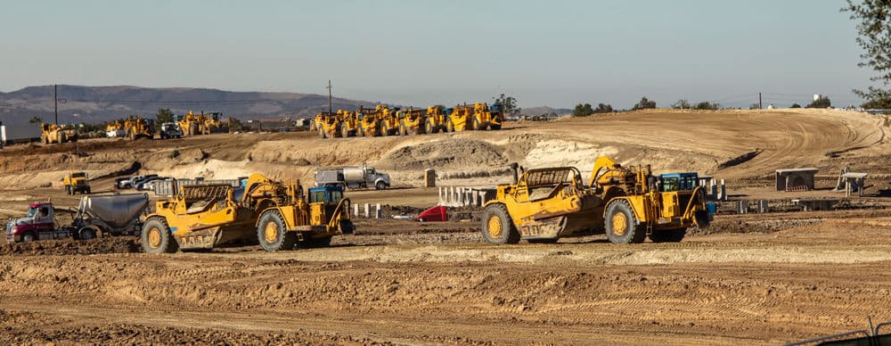 Construction site with yellow heavy machinery and equipment on dirt landscape.
